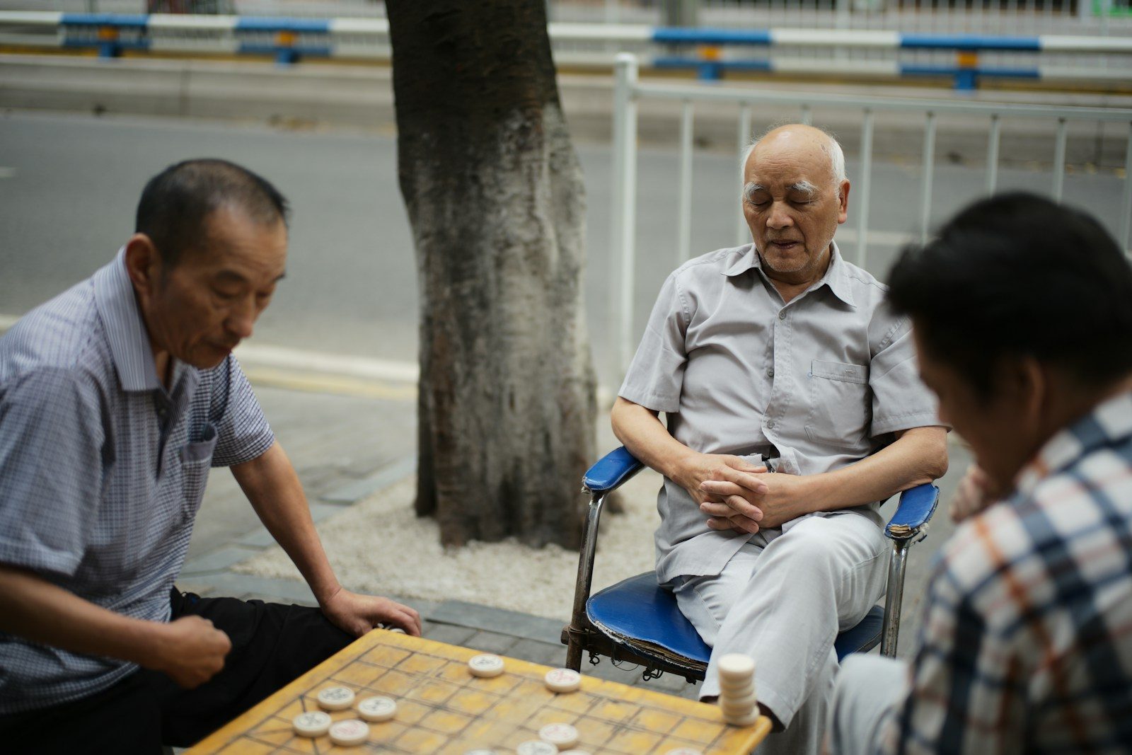 Three elderly men playing a board game outdoors