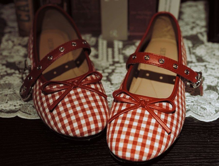 A pair of red and white gingham flats with bows on a lace doily